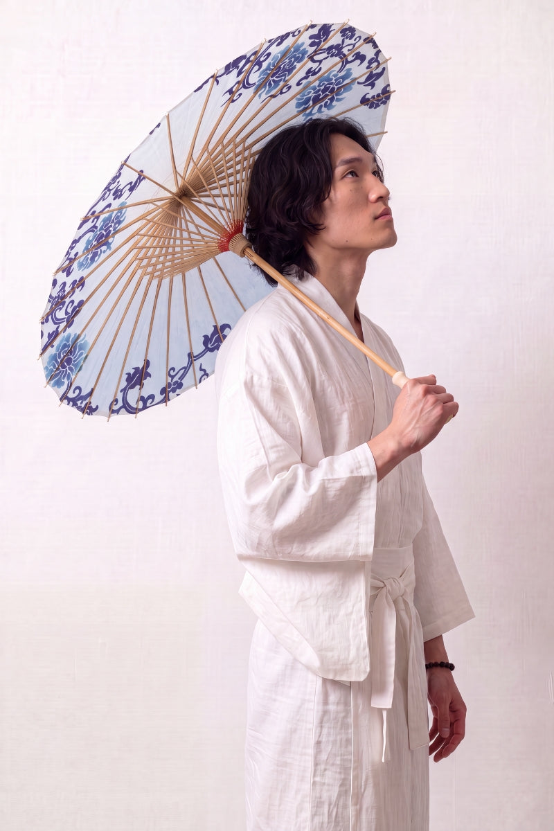 Traditional Japanese paper umbrella with stylized navy and pale blue flowers ringing a bright white canopy, held open overhead by a model in a white kimono