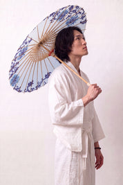 Traditional Japanese paper umbrella with stylized navy and pale blue flowers ringing a bright white canopy, held open overhead by a model in a white kimono