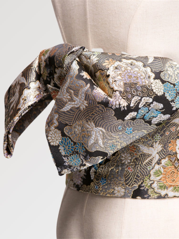 Black brocade obi belt with silver chrysanthemums, cranes and waves in blue, green and orange, close detail of the woven fabric and pattern