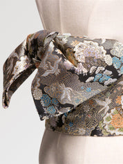 Black brocade obi belt with silver chrysanthemums, cranes and waves in blue, green and orange, close detail of the woven fabric and pattern