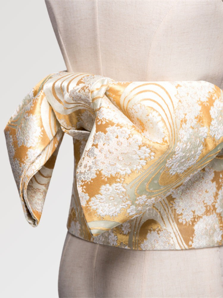 Soft gold obi belt woven with white blossom clusters and flowing-water lines, close detail of the woven fabric and pattern